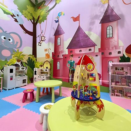 Evergreen Laurel Hotel - Taichung Extérieur photo The photo shows a colorful children's playroom designed with a whimsical theme. The walls are painted in bright colors and feature a cartoon-style mural of a pink castle with purple towers and a smiling cartoon elephant. The room is filled with playf