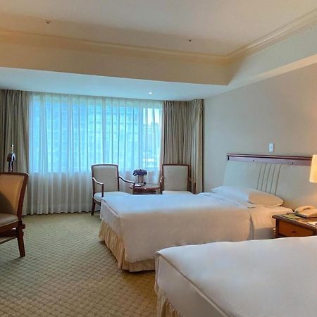 Evergreen Laurel Hotel - Taichung Extérieur photo The photo shows a hotel room featuring two single beds positioned near each other. There's a light-colored carpet on the floor and a large window with sheer curtains that allows natural light to fill the space. In the room, there are two chairs place