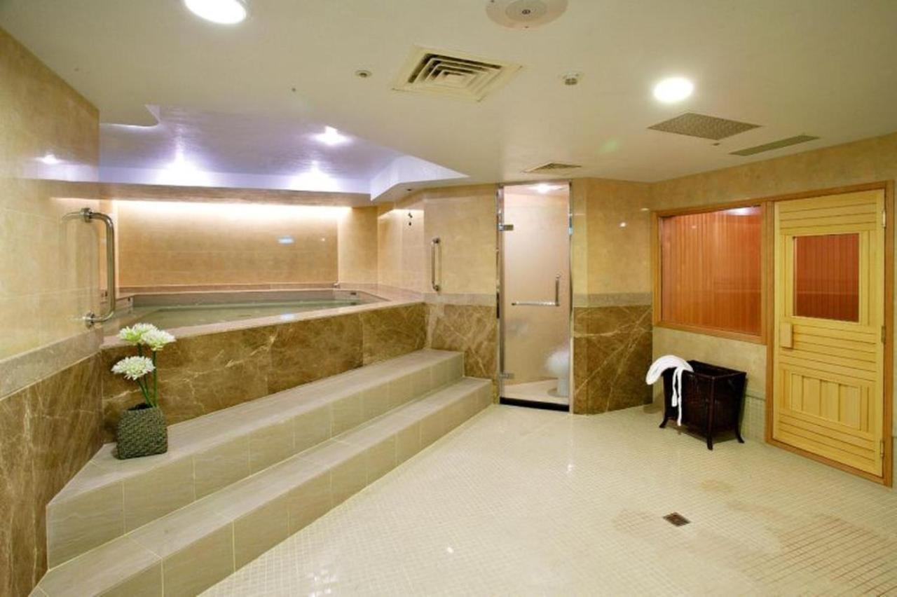 Evergreen Laurel Hotel - Taichung Extérieur photo The photo shows a spacious and well-lit spa or wellness area. It features a large, recessed hot tub with steps leading up to it, surrounded by beige marble walls. There's a shower area enclosed in glass, and to the right, a wooden sauna or steam room