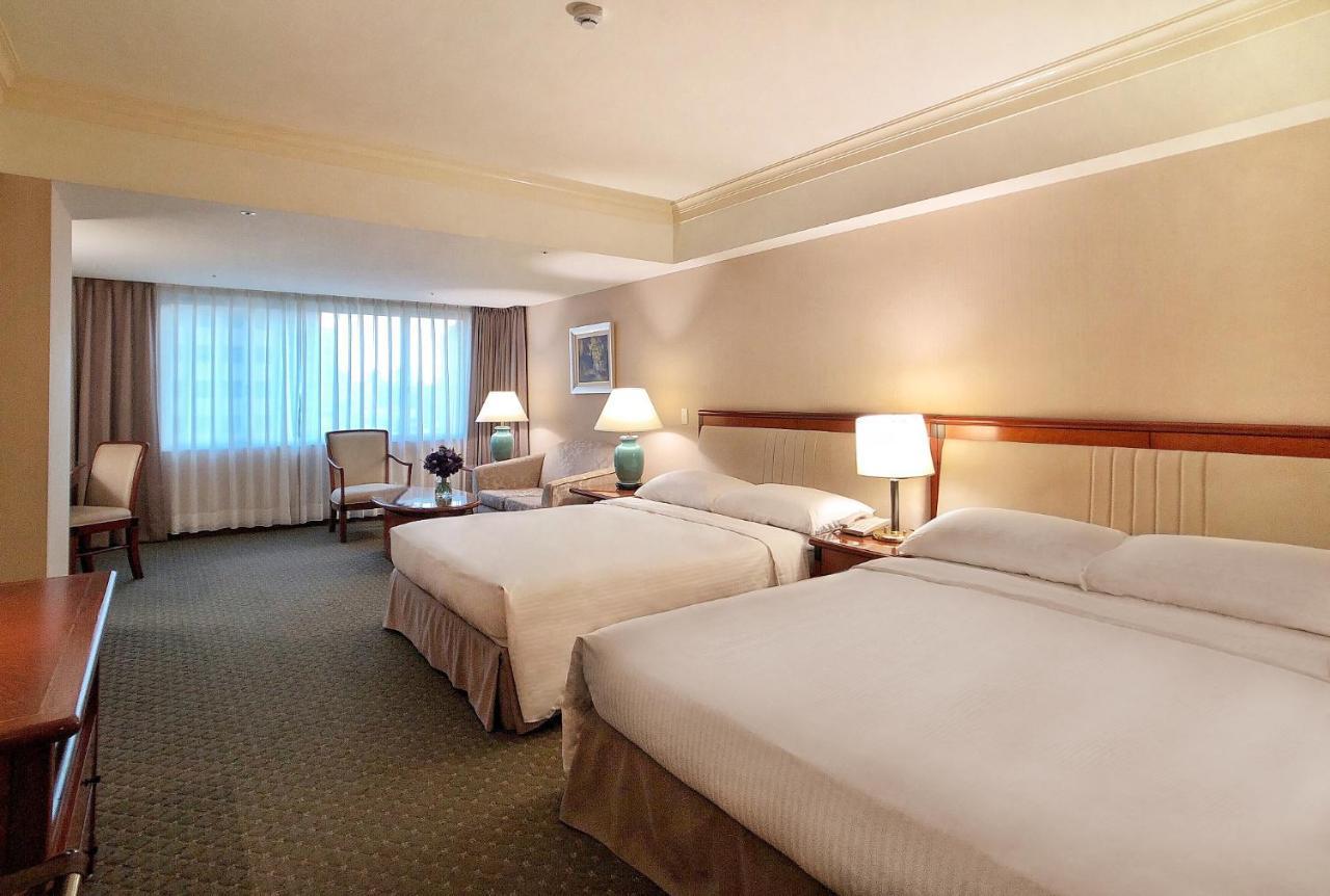 Evergreen Laurel Hotel - Taichung Extérieur photo The photo shows a hotel room featuring two queen-sized beds with white linens. The room is well-lit and has a warm, neutral color palette. There are bedside lamps on each side of the beds and a small table. To the side, there's a comfortable armchair