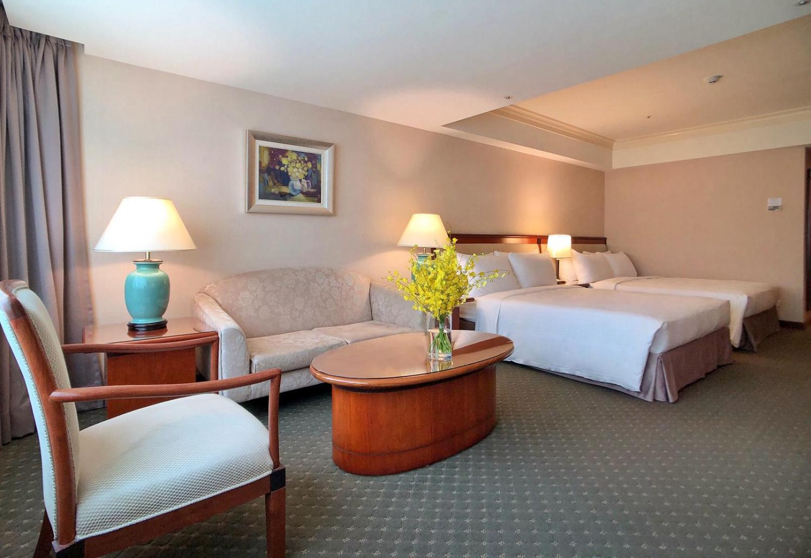 Evergreen Laurel Hotel - Taichung Extérieur photo The photo shows a hotel room featuring two beds, a small seating area, and a coffee table. The walls are painted in soft, neutral colors, and there is a framed piece of artwork hanging on the wall. A potted plant with yellow flowers is placed on the 