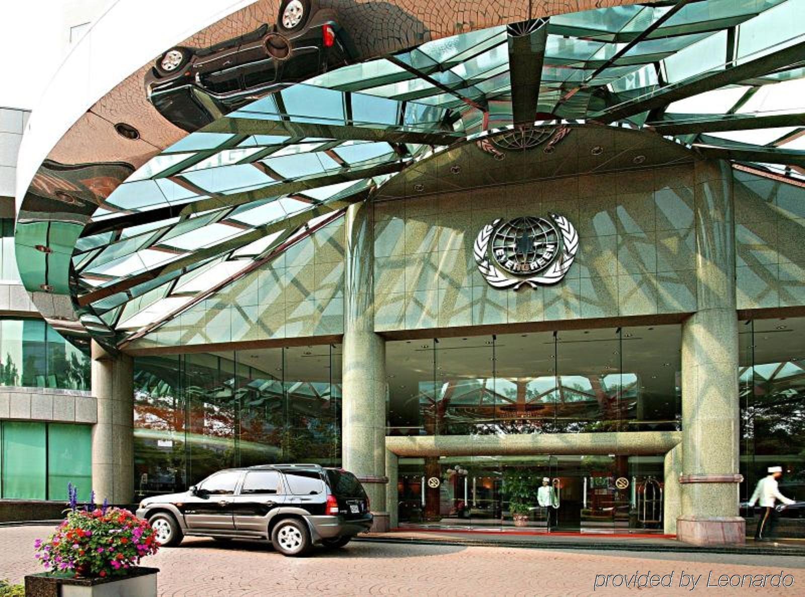 Evergreen Laurel Hotel - Taichung Extérieur photo The photo shows the entrance of a modern building characterized by its glass and metal architecture. The structure features a large, domed roof that reflects light, with a distinctive emblem or logo displayed prominently at the center. In front of th