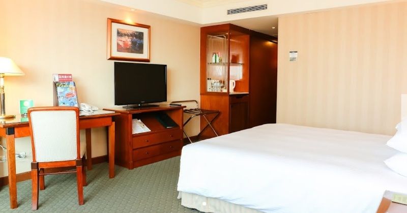 Evergreen Laurel Hotel - Taichung Extérieur photo The photo shows a hotel room featuring a neatly made bed with a white blanket. On one side, there is a wooden desk with a chair, and a flat-screen television is mounted nearby. An accent cabinet is visible, displaying various items. The walls are pai