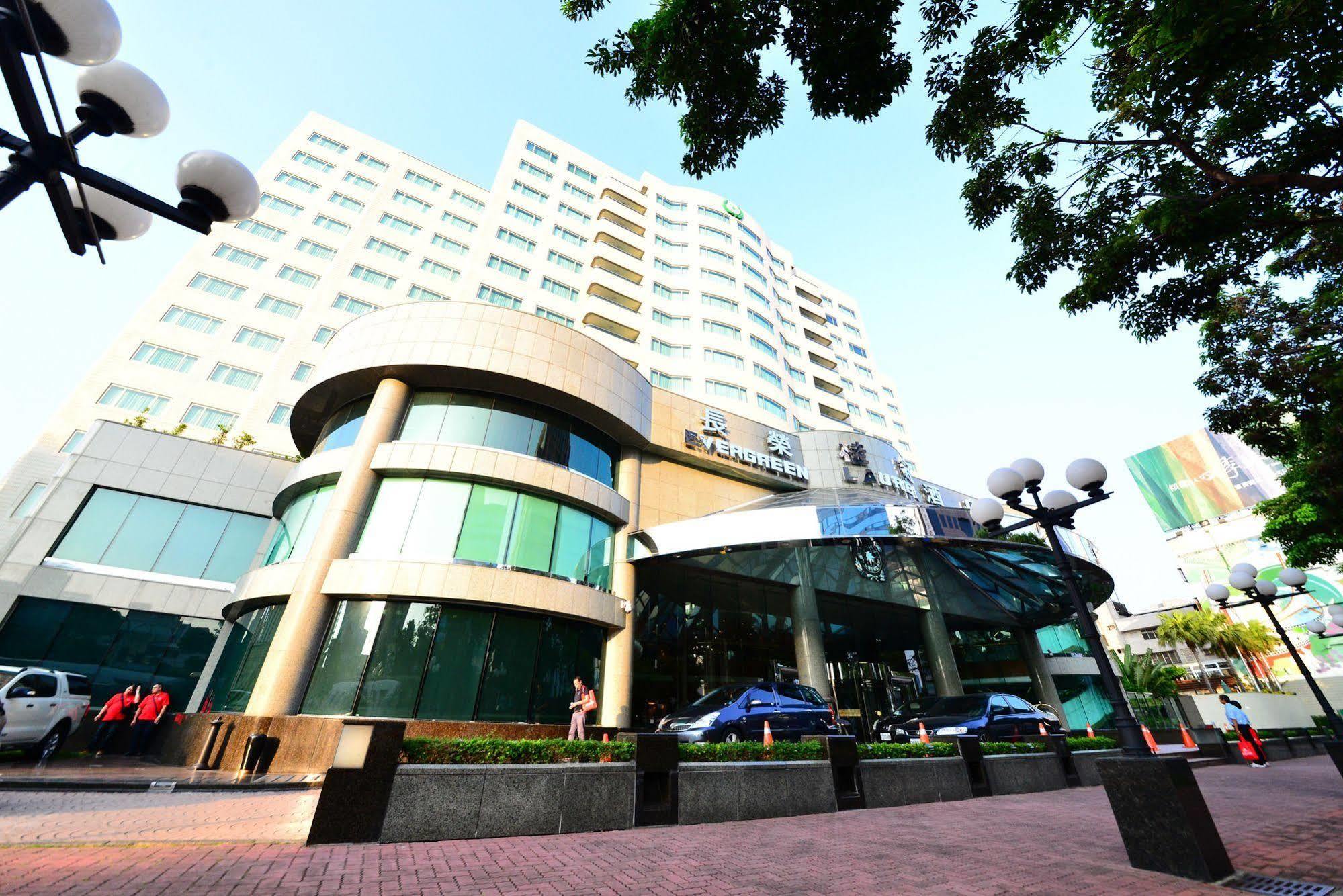 Evergreen Laurel Hotel - Taichung Extérieur photo The photo shows a modern multi-story building, which appears to be a hotel or commercial establishment. The structure has a rounded glass entrance with a distinctive architectural design, featuring large windows. The building is surrounded by greener