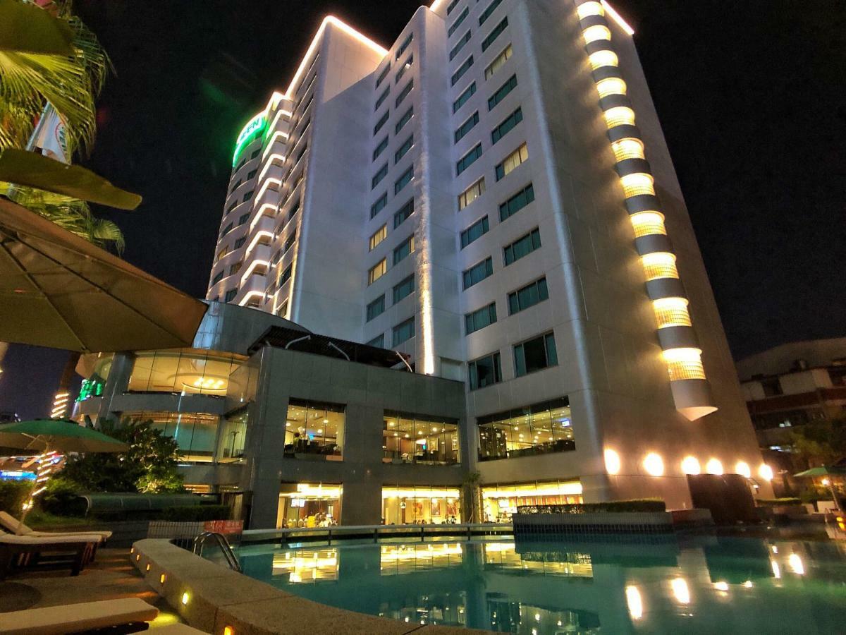 Evergreen Laurel Hotel - Taichung Extérieur photo The photo shows a tall hotel building at night, illuminated by lights. The architecture appears modern, with several floors and large windows. In the foreground, there is a swimming pool that reflects the lights from the building, creating a serene a