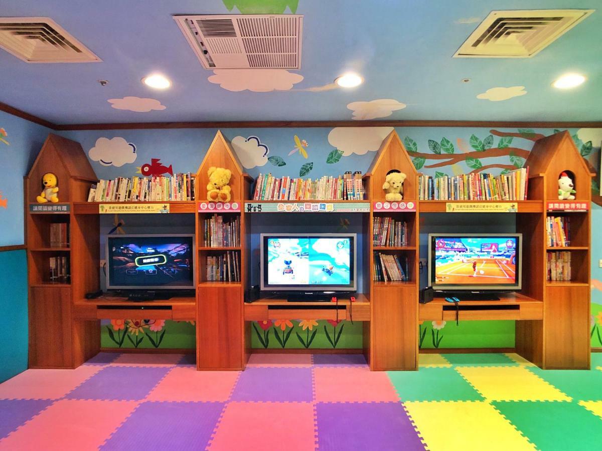 Evergreen Laurel Hotel - Taichung Extérieur photo The photo shows a colorful and playful room designed for children. In the center, there are three wooden gaming stations, each equipped with a television screen and surrounded by shelves filled with books. The walls are decorated with cheerful images