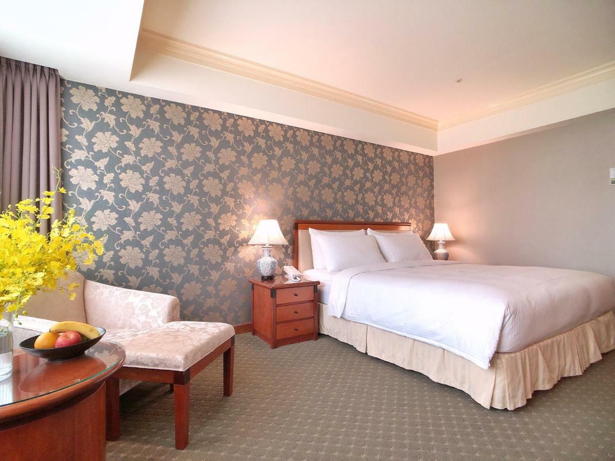 Evergreen Laurel Hotel - Taichung Extérieur photo The photo shows a well-decorated hotel room. It features a large bed with white bedding, situated against a patterned wall with floral designs. On either side of the bed are bedside tables with lamps. There is a small seating area that includes a cha