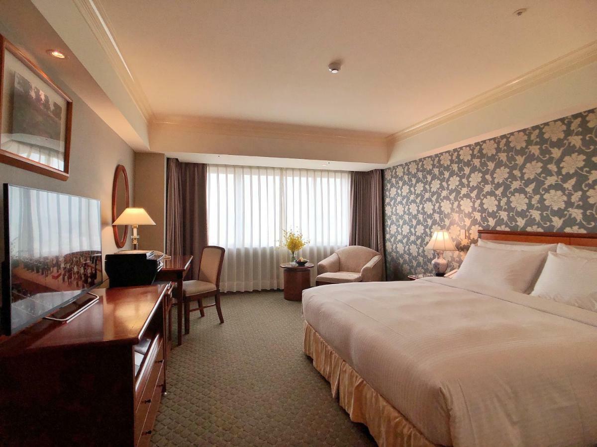 Evergreen Laurel Hotel - Taichung Extérieur photo The photo shows a hotel room with a spacious layout. It features a large bed with white bedding, bedside lamps, and a decorative headboard. There is a comfortable seating area with an armchair and small table. A desk is present, complete with a lamp 
