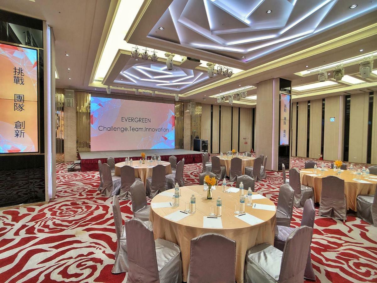 Evergreen Laurel Hotel - Taichung Extérieur photo The photo shows a conference or event space set up for a gathering. The room features several round tables with light-colored tablecloths and chairs, each with decoration, possibly for dining or discussion. A large screen displays the text "EVERGREEN
