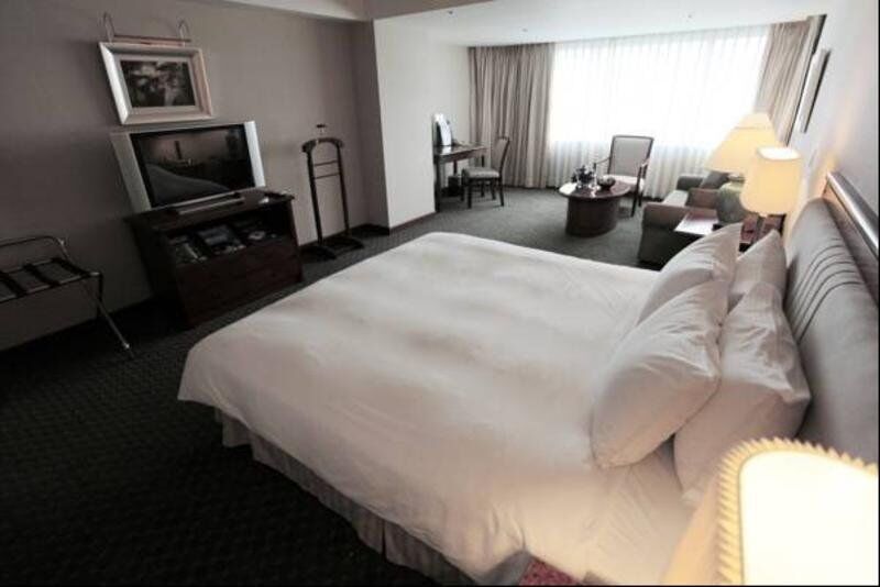 Evergreen Laurel Hotel - Taichung Extérieur photo The photo shows a hotel room featuring a large bed with white bedding. There is a flat-screen television on a wooden cabinet opposite the bed. Nearby, there are two armchairs and a small table, creating a cozy seating area. Large windows allow natura