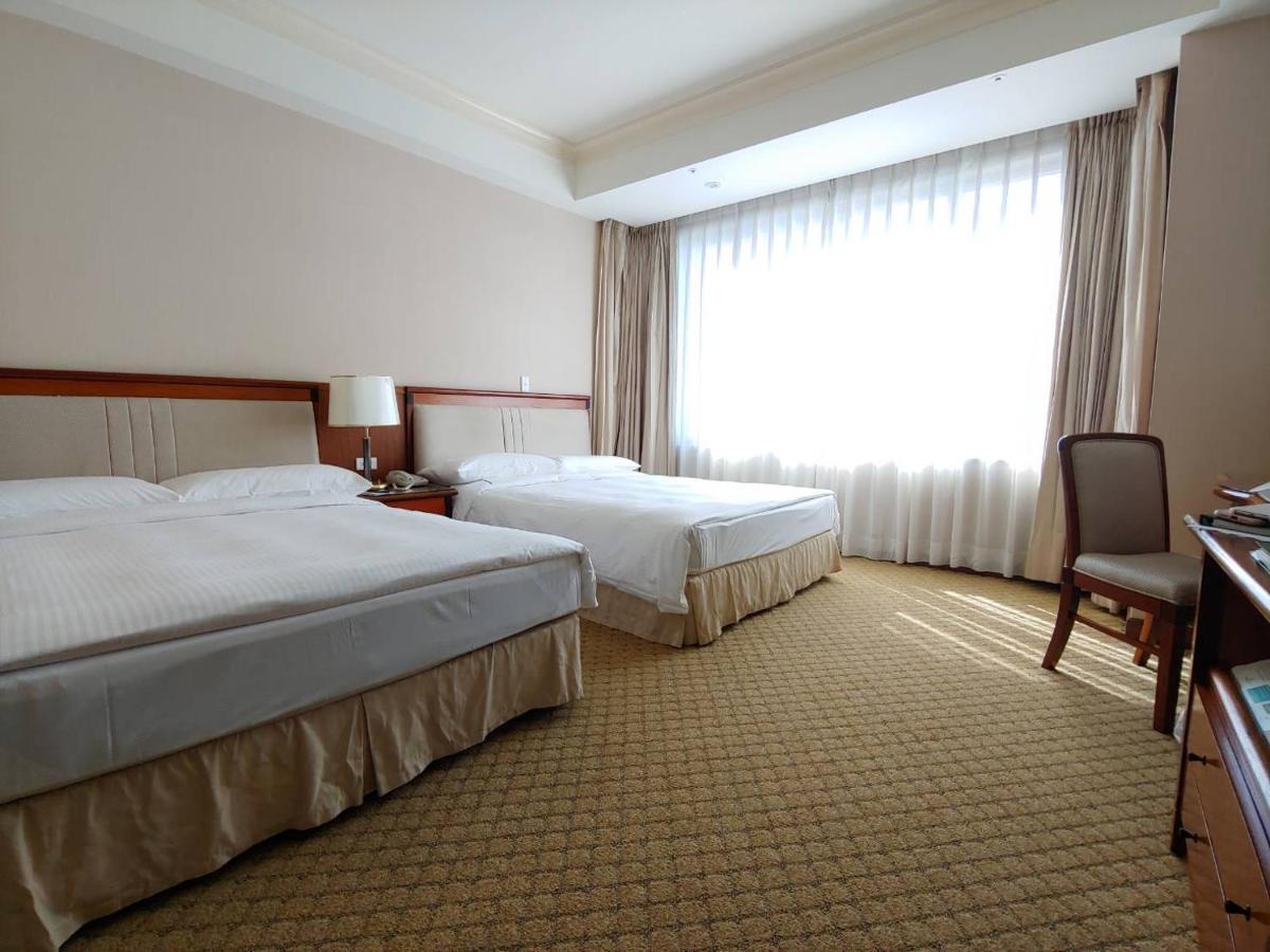 Evergreen Laurel Hotel - Taichung Extérieur photo The photo shows a neatly arranged hotel room featuring two beds: one double bed and one single bed. The room has beige walls and a warm color palette. Large windows with sheer curtains allow natural light to flood in, creating a bright and airy atmos