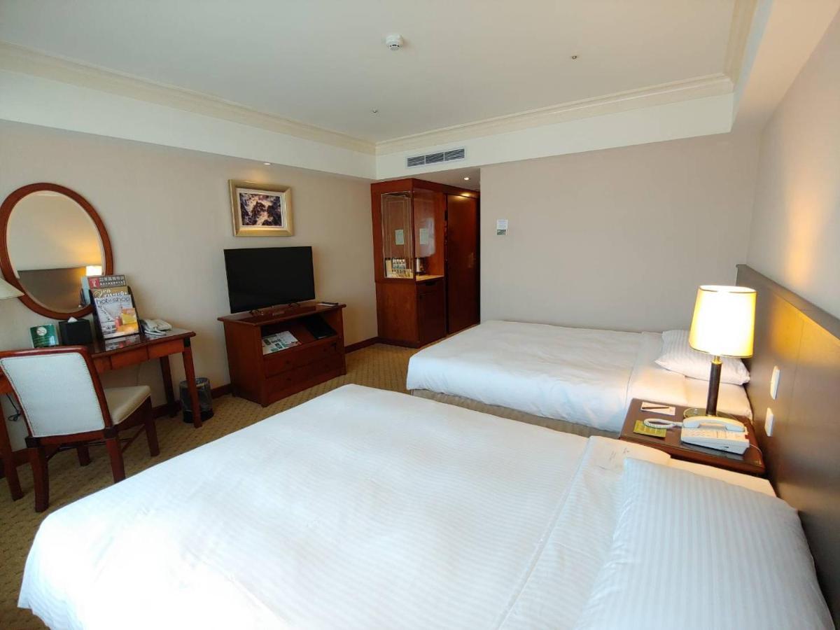 Evergreen Laurel Hotel - Taichung Extérieur photo The photo shows a hotel room with two beds, neatly made with white linens. There is a desk and chair in one corner, accompanied by a flat-screen TV mounted on the wall. A large mirror and a wooden cabinet are also visible. The room is illuminated by 